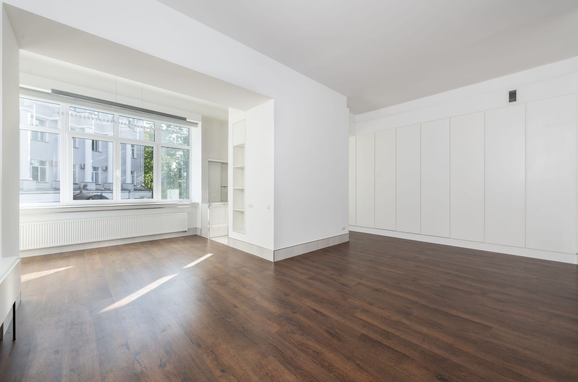 Pièce d’appartement vide et lumineuse, parquet impeccable et grandes fenêtres baignées de soleil