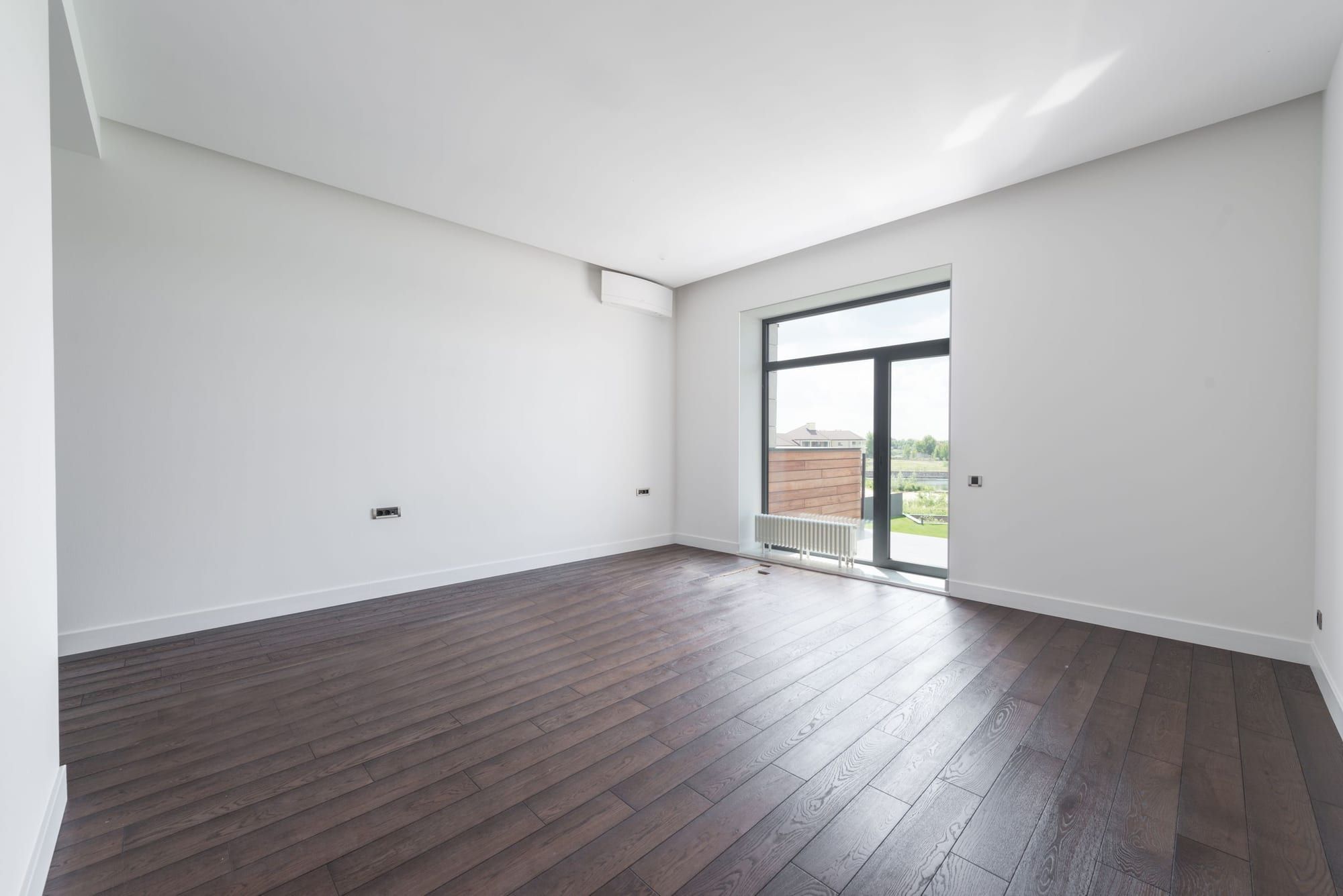 Pièce vide et propre avec parquet foncé et porte-fenêtre donnant sur l’extérieur